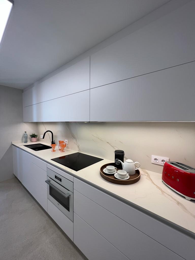 Cocina blanca lineal con muebles bajos y altos colgados elevables