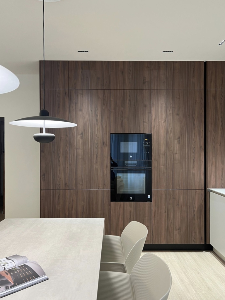 Cocina en Gandia en L en color Perla y Columnas en Nogal Vitrina de cristal en mueble alto colgado en blanco y marco en negro con copas en el interior